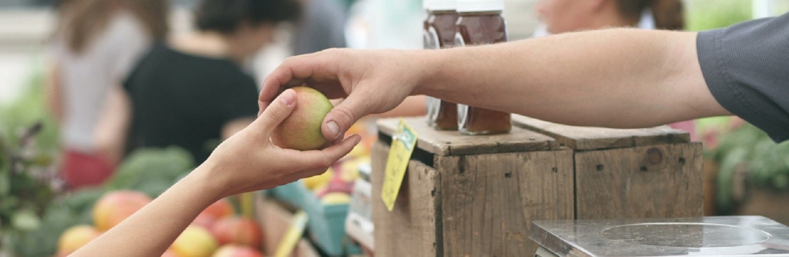 unidentified person at farmers market handing a customer an apple