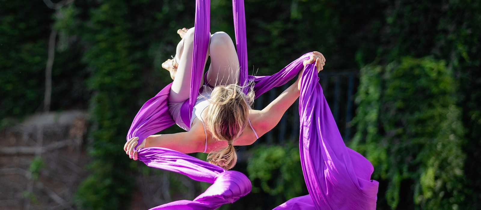 young woman suspended in the air on two purple lengths of cloth