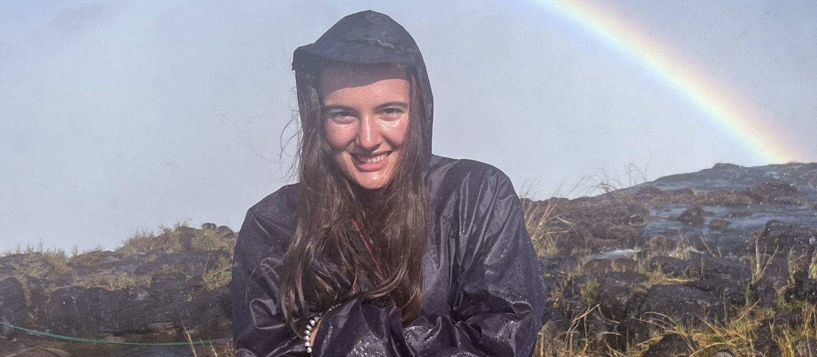 young woman in a raincoat with a rainbow behind her