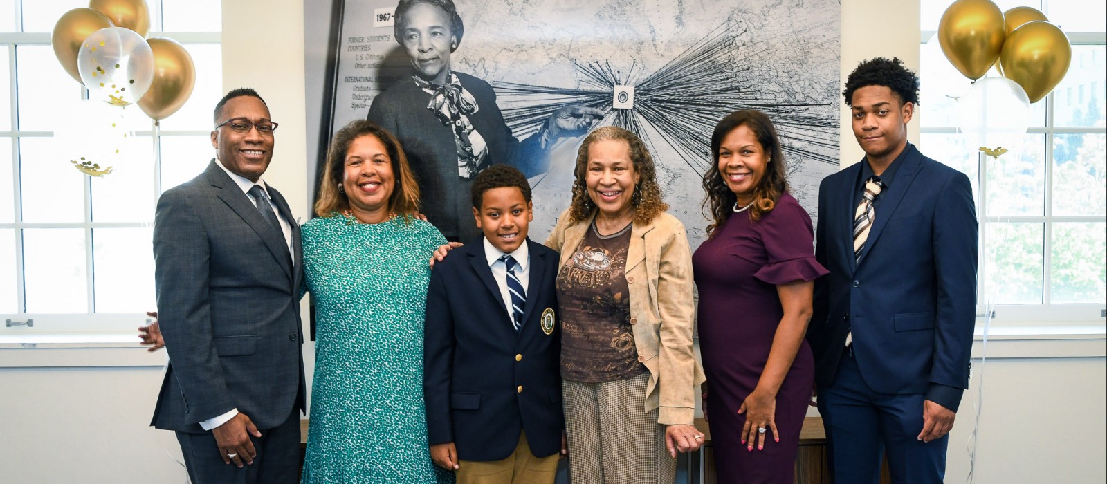 Six members of the Kittrell family stand in front of a portrait of Flemmie Kittrell.