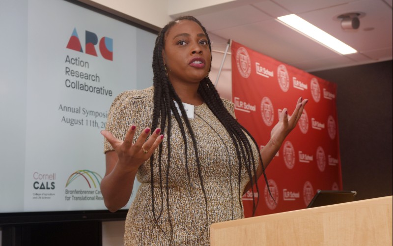 person with long braids gesturing as they speak at a podium