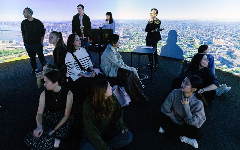 group of people in a projection room with an aerial image of NYC behind them