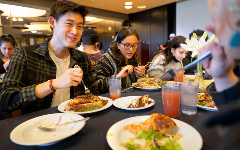 students sitting at a dining hall table eating a meal