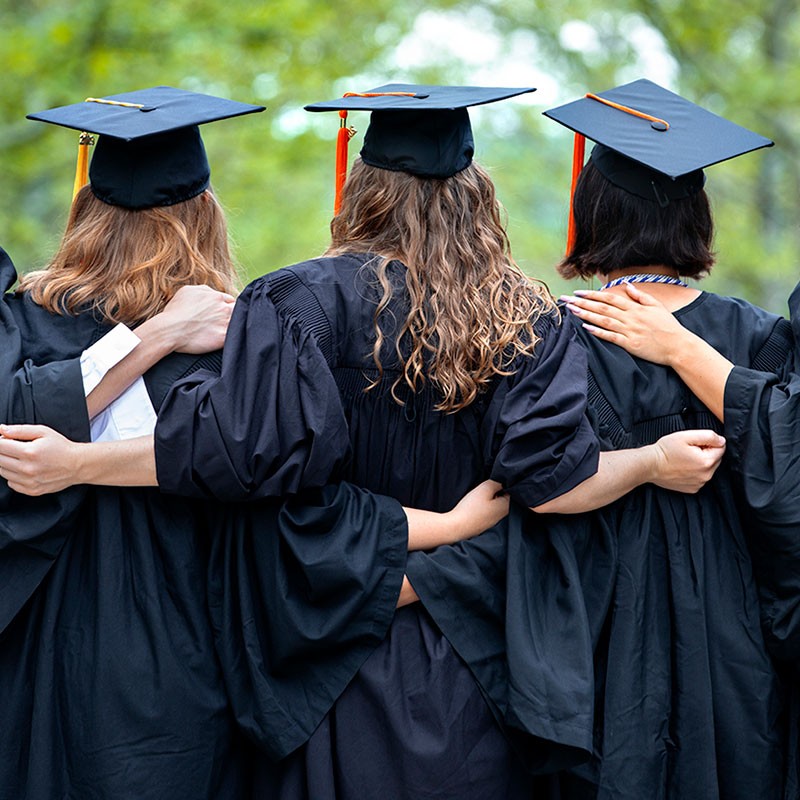 graduates in cap and gown with arms around each others' shoulders