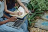 unrecognizable diverse female students working on laptop outdoors on park bench